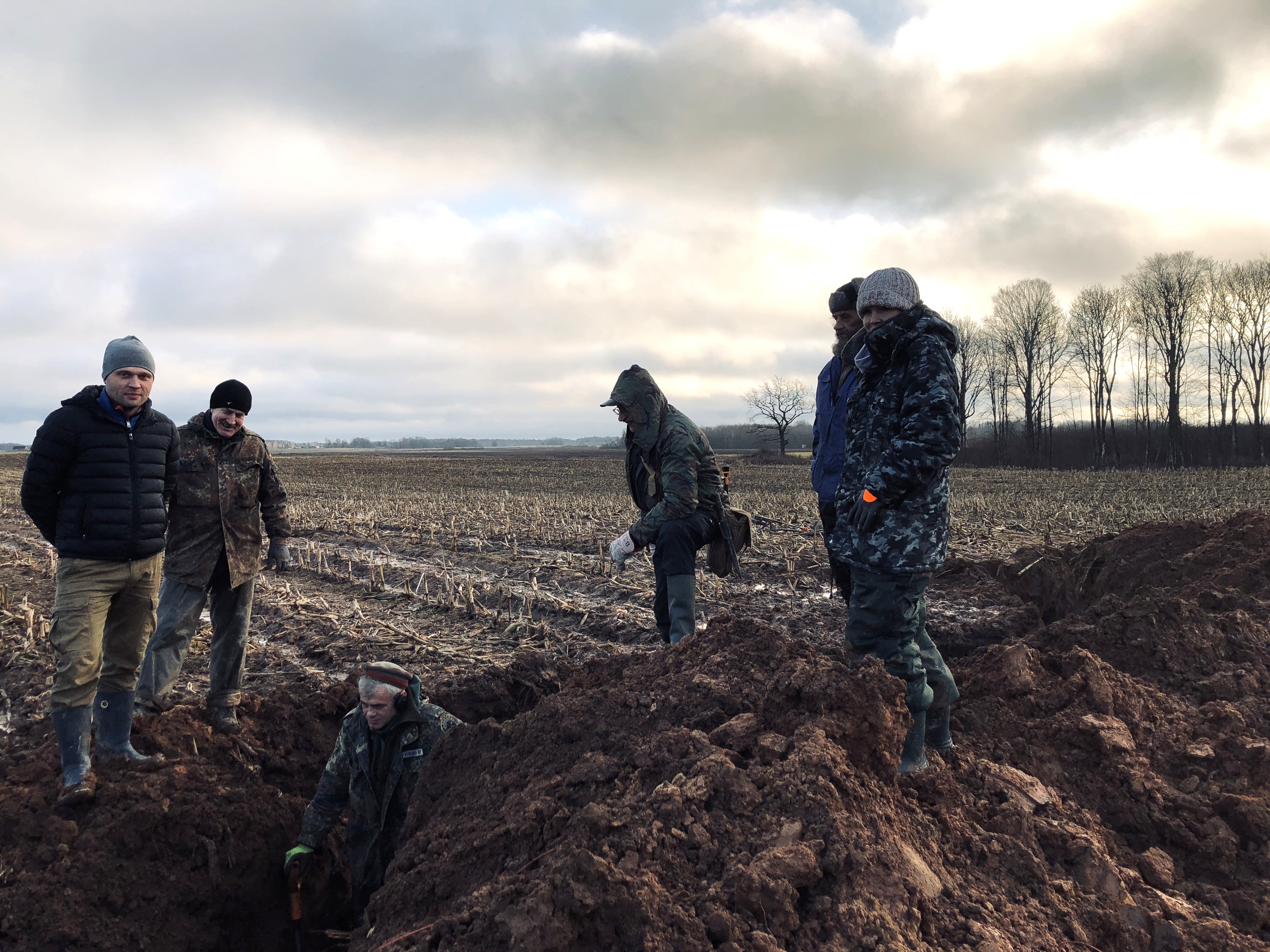 Volunteers of Legenda gathered around an open dig in a Latvian field under a heavy sky